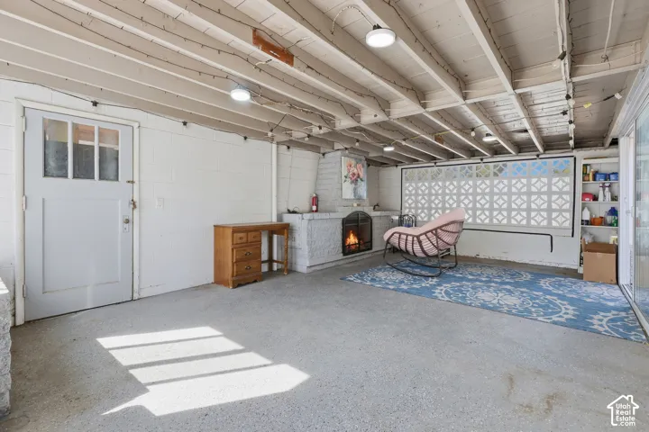 Exposed wood beam ceiling, white-painted brick fireplace, built-in shelving, glass-paneled door, and concrete flooring