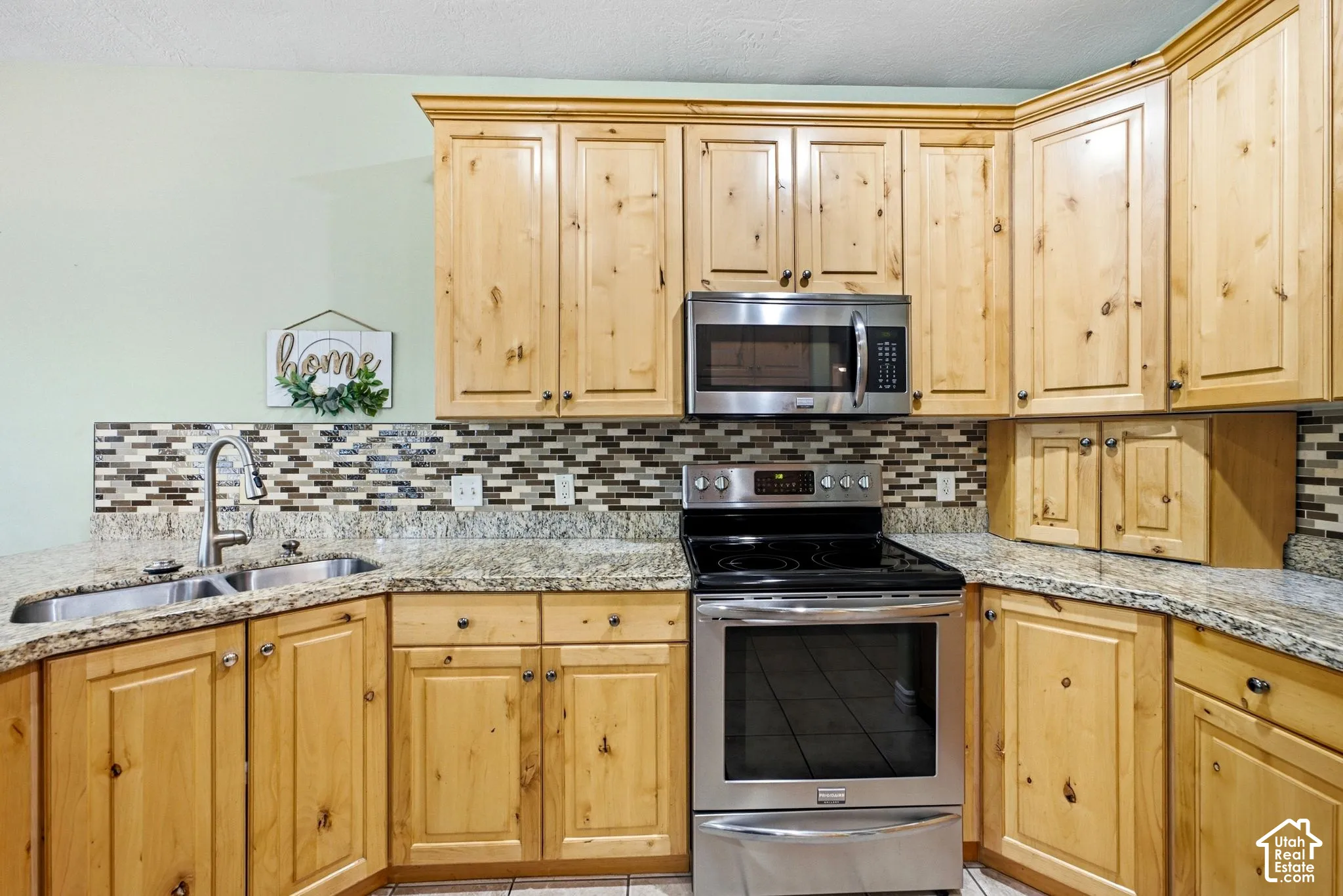 Kitchen featuring wood cabinetry, stainless steel appliances, granite-style countertops, mosaic tile backsplash, and a double basin sink