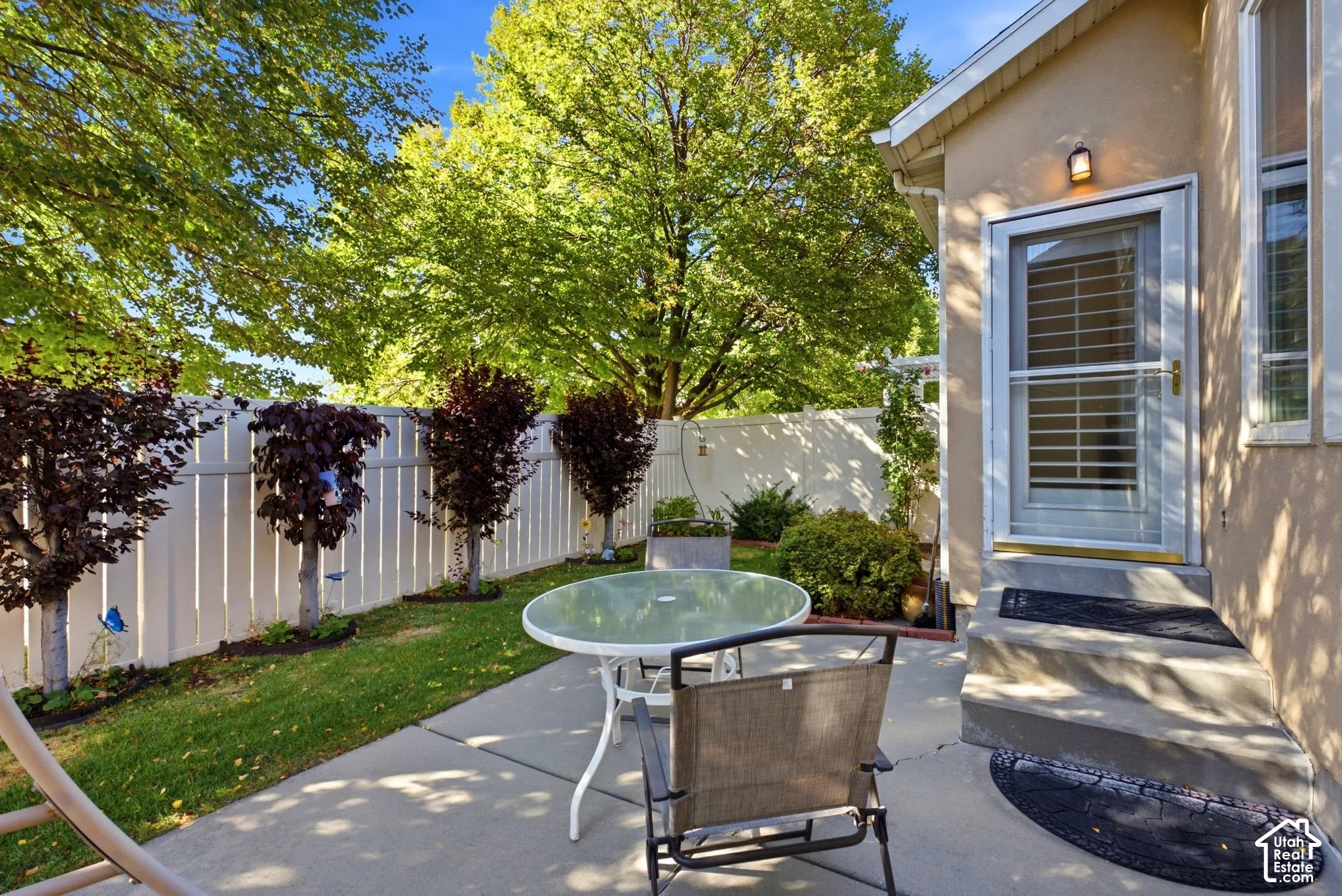 Private rear patio with concrete surfacing, white privacy fencing, mature trees, and an exterior door with screen