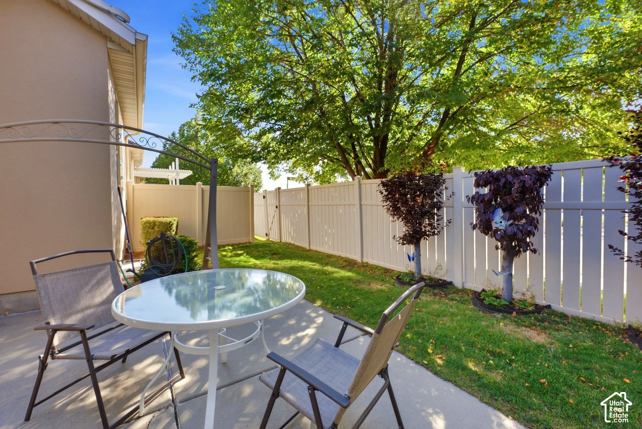 Concrete patio with adjacent grass area, bordered by a white privacy fence and established trees