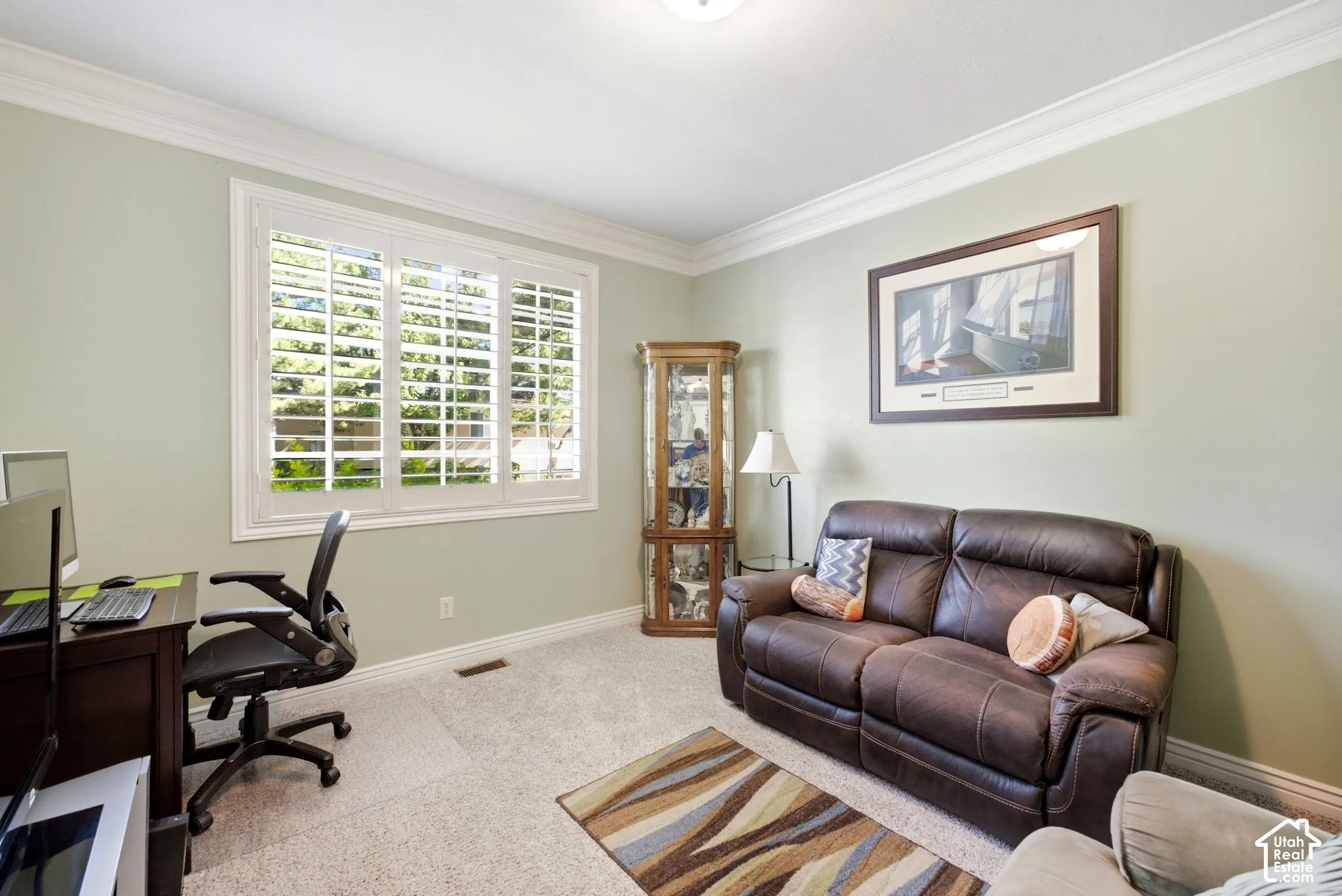 Window with interior shutters, crown molding, light-toned carpeting, and a built-in display cabinet