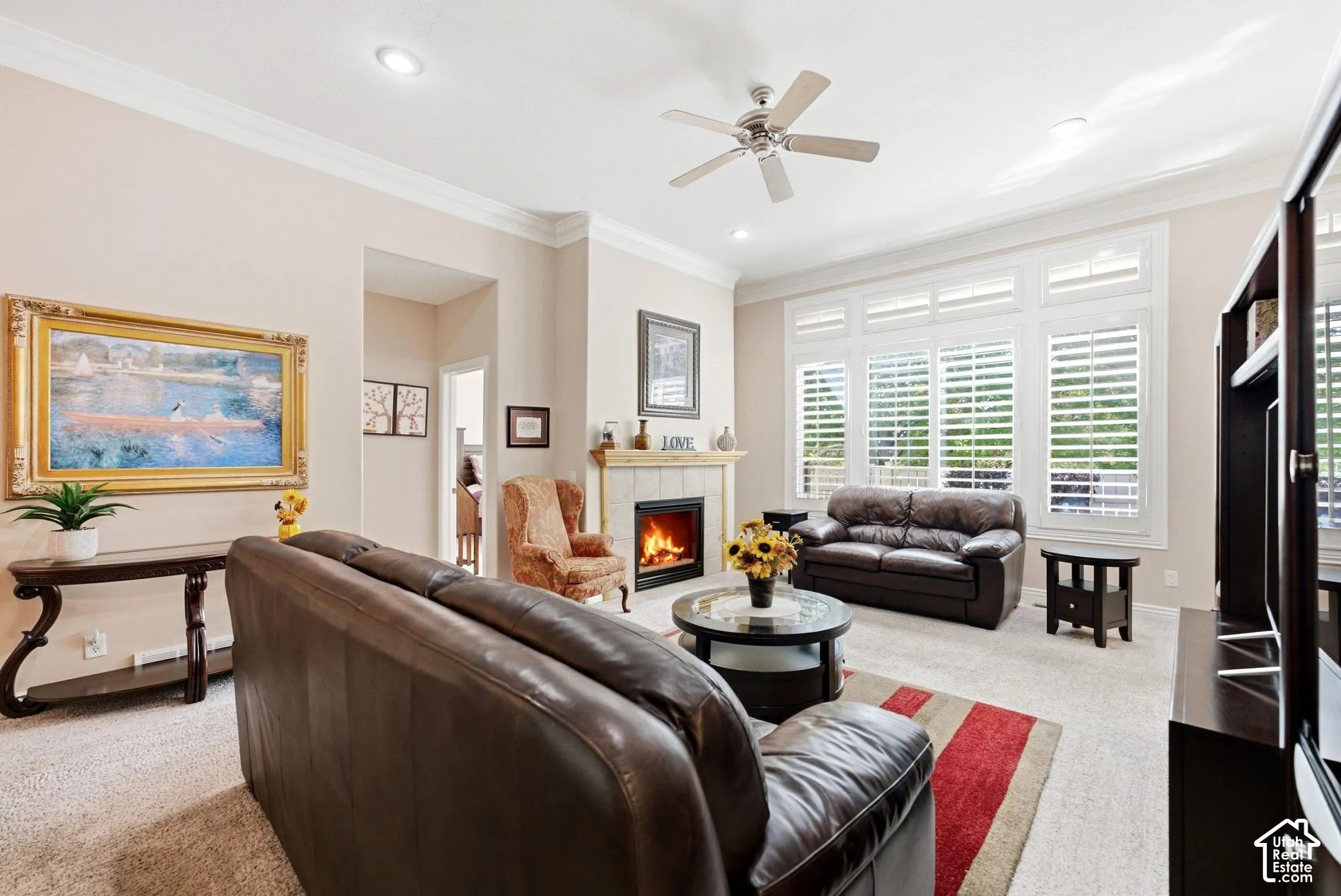 Living area featuring a fireplace with a mantel, recessed lighting, crown molding, a ceiling fan, and large windows with plantation shutters