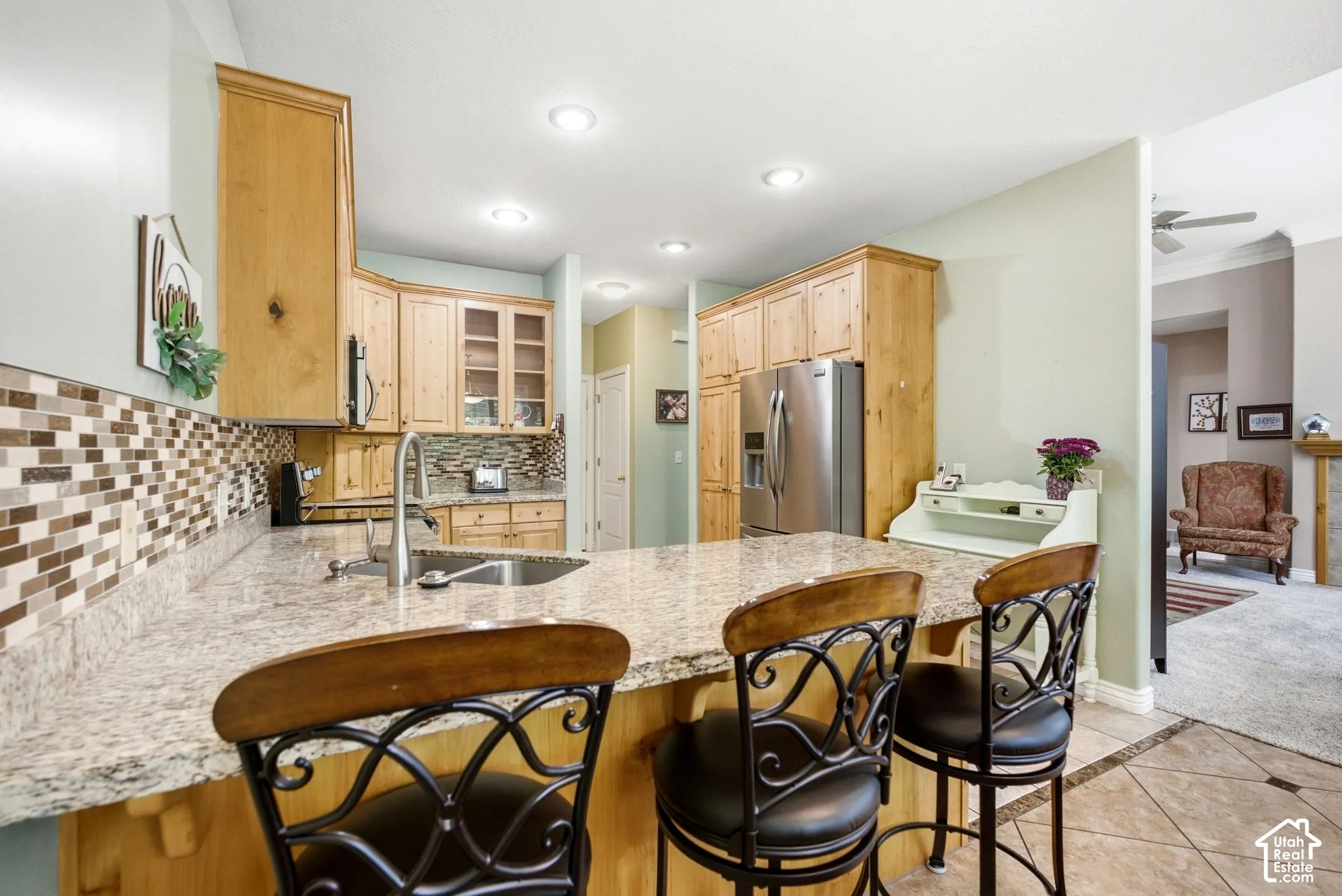Kitchen featuring wood cabinetry, stainless steel appliances, a multi-tone tile backsplash, a kitchen island with seating, and recessed lighting