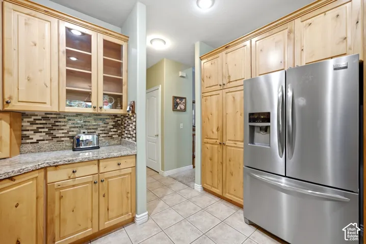 Wood-finish cabinetry, tile flooring, stone-finish countertops, glass-front upper cabinets, and a stainless steel refrigerator