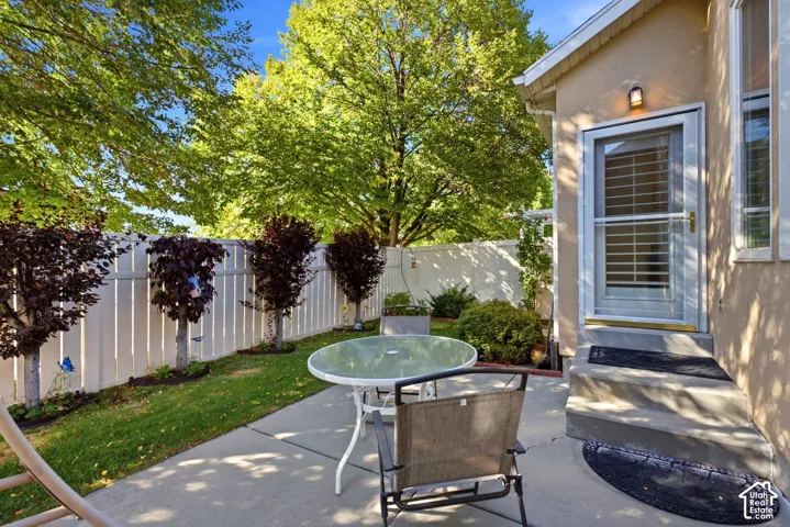 Private rear patio with concrete surfacing, white privacy fencing, mature trees, and an exterior door with screen