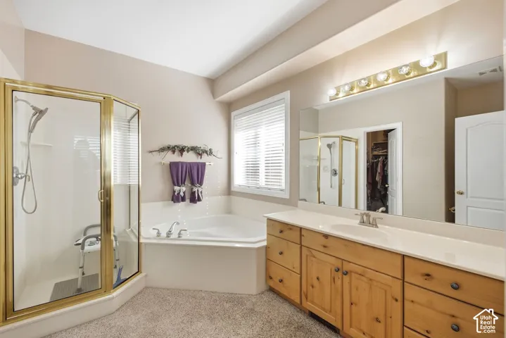 Corner soaking tub, enclosed shower, light wood-finish vanity with dual sinks, wall-mounted mirror, and vanity lighting