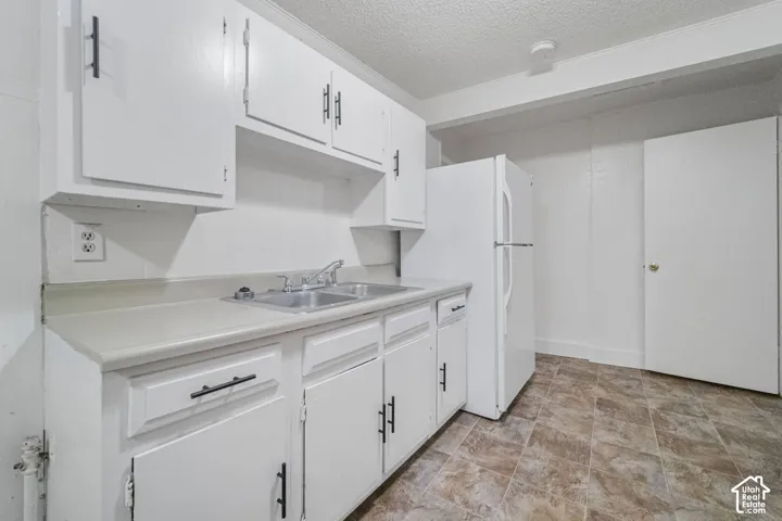 White cabinetry with black hardware, double basin stainless steel sink, light-toned countertop, and patterned flooring