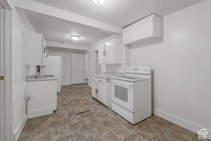 White kitchen cabinetry with black hardware, complementing white appliances, and a durable tile flooring