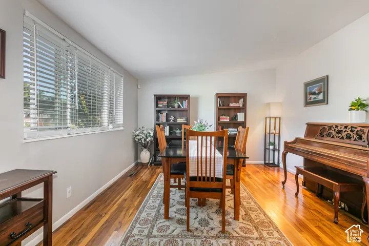 Living area featuring wood-finish flooring, white walls, and a large window with horizontal blinds