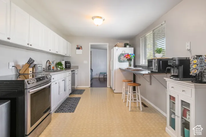 Kitchen featuring white cabinetry, stainless steel appliances, a built-in folding counter, a window, and wood-finish flooring