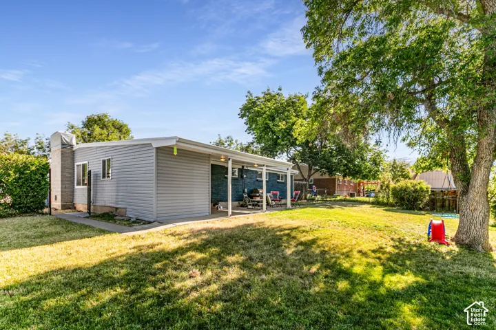 Expansive backyard featuring a large green space, mature shade trees, and a covered patio area