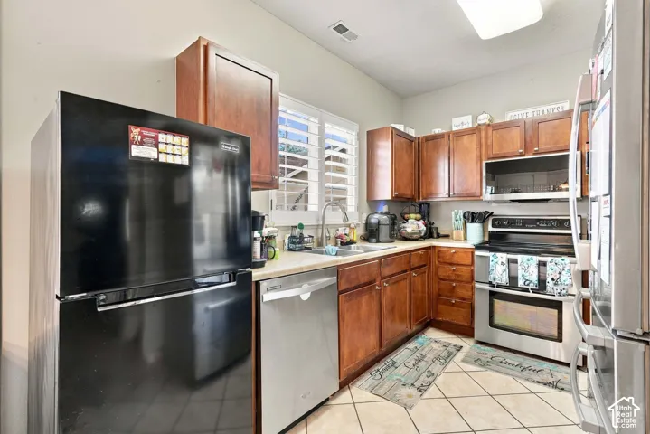 Kitchen featuring wood cabinetry, light-toned countertops, a stainless steel dishwasher, a stainless steel range with overhead microwave, and tiled flooring  This black fridge is EXCLUDED.