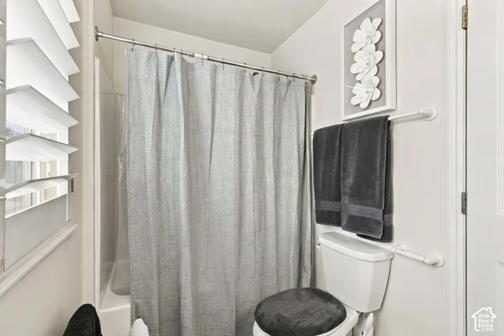 Primary Ensuite White bathtub and shower combination with a chrome shower rod, a white toilet, and interior plantation shutters