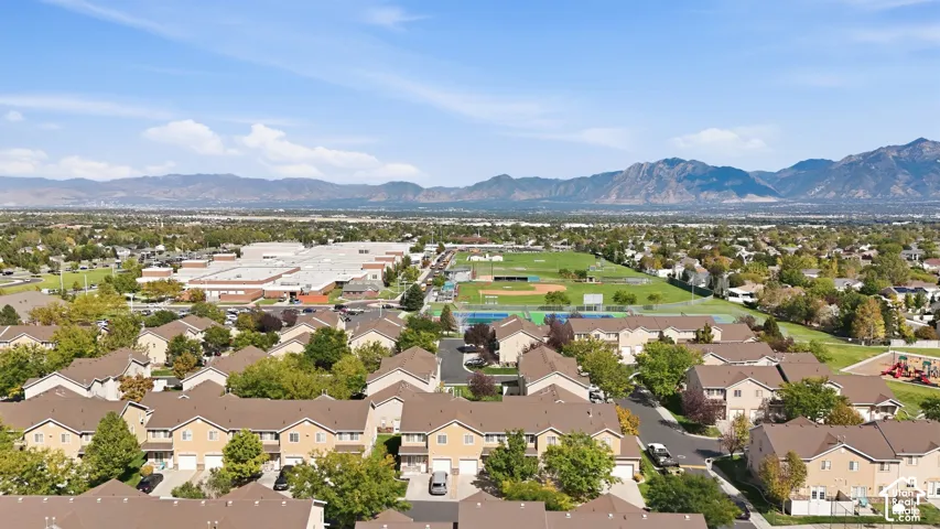 Expansive mountain backdrop, residential community, multiple sports fields, large institutional building, and clear skies