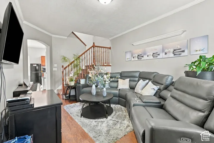 Wood-finish flooring, staircase with wood banister and white risers, arched entryway, crown molding, and recessed lighting