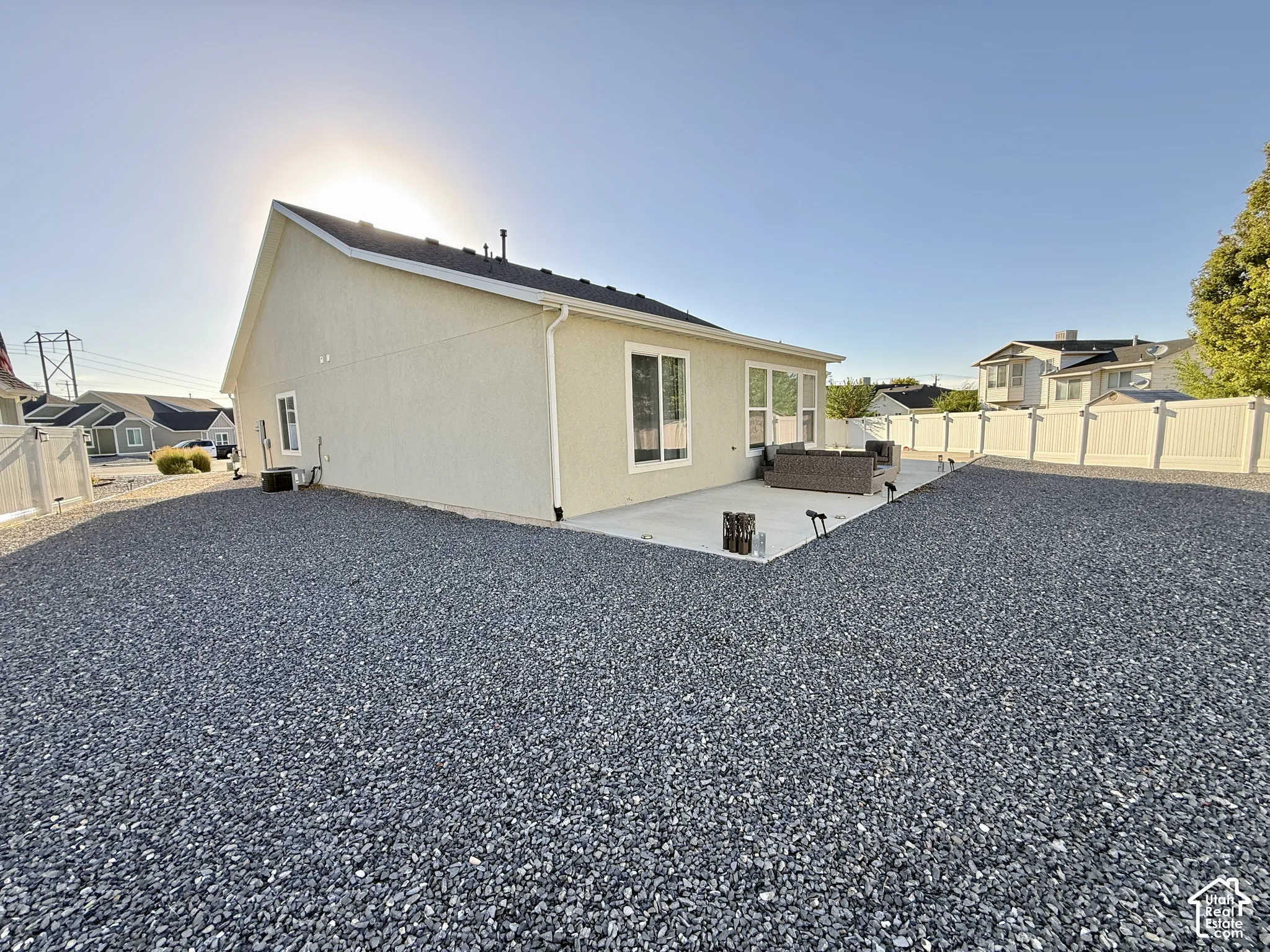 Exterior stucco finish, rear concrete patio, white privacy fencing, and gravel landscaping