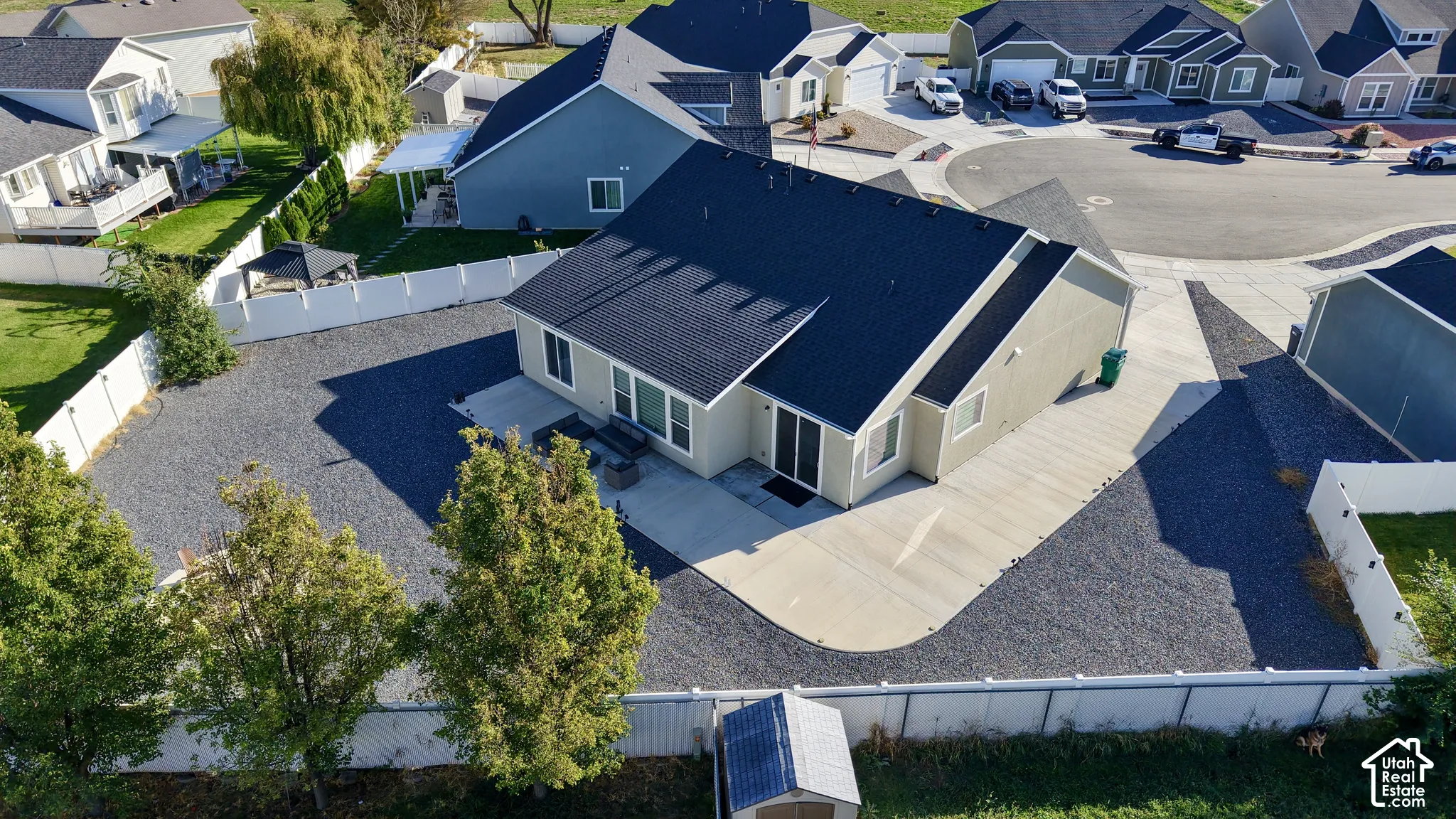 Rear exterior with concrete patio, sliding glass door, white perimeter fencing, and gravel landscaping