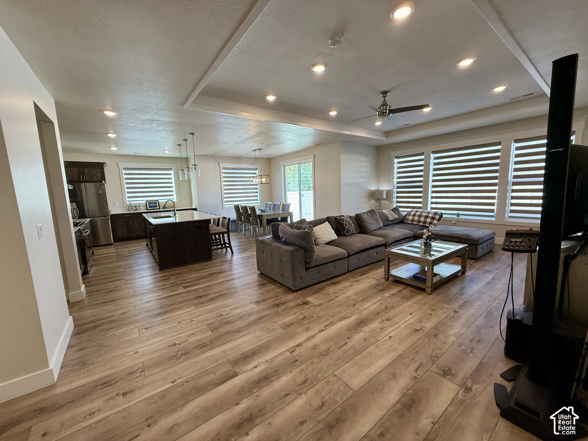 Open-concept living space with wood-finish flooring, recessed lighting, and a tray ceiling