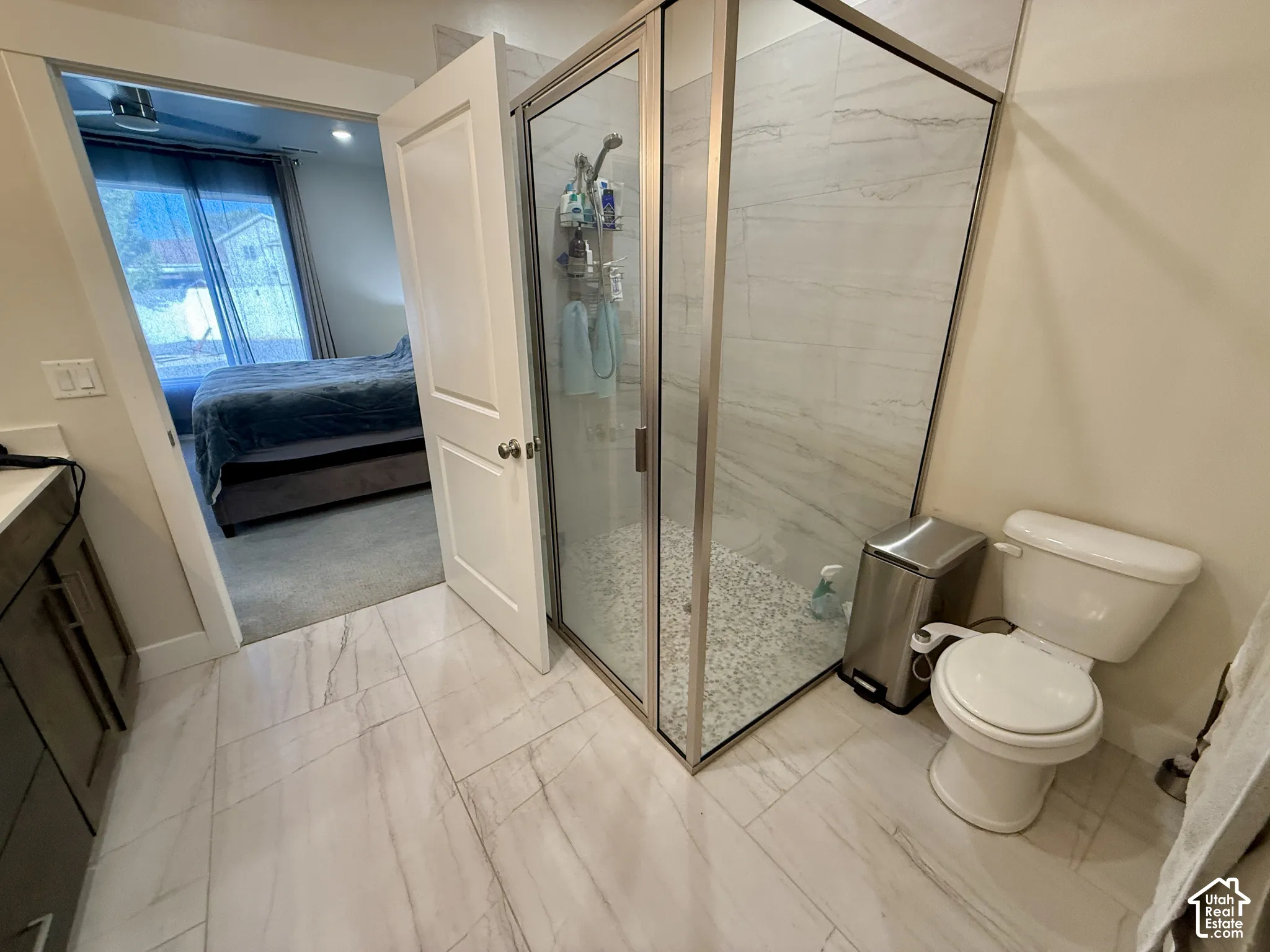 Walk-in shower with clear glass enclosure and pebble flooring, large format tile flooring, white toilet