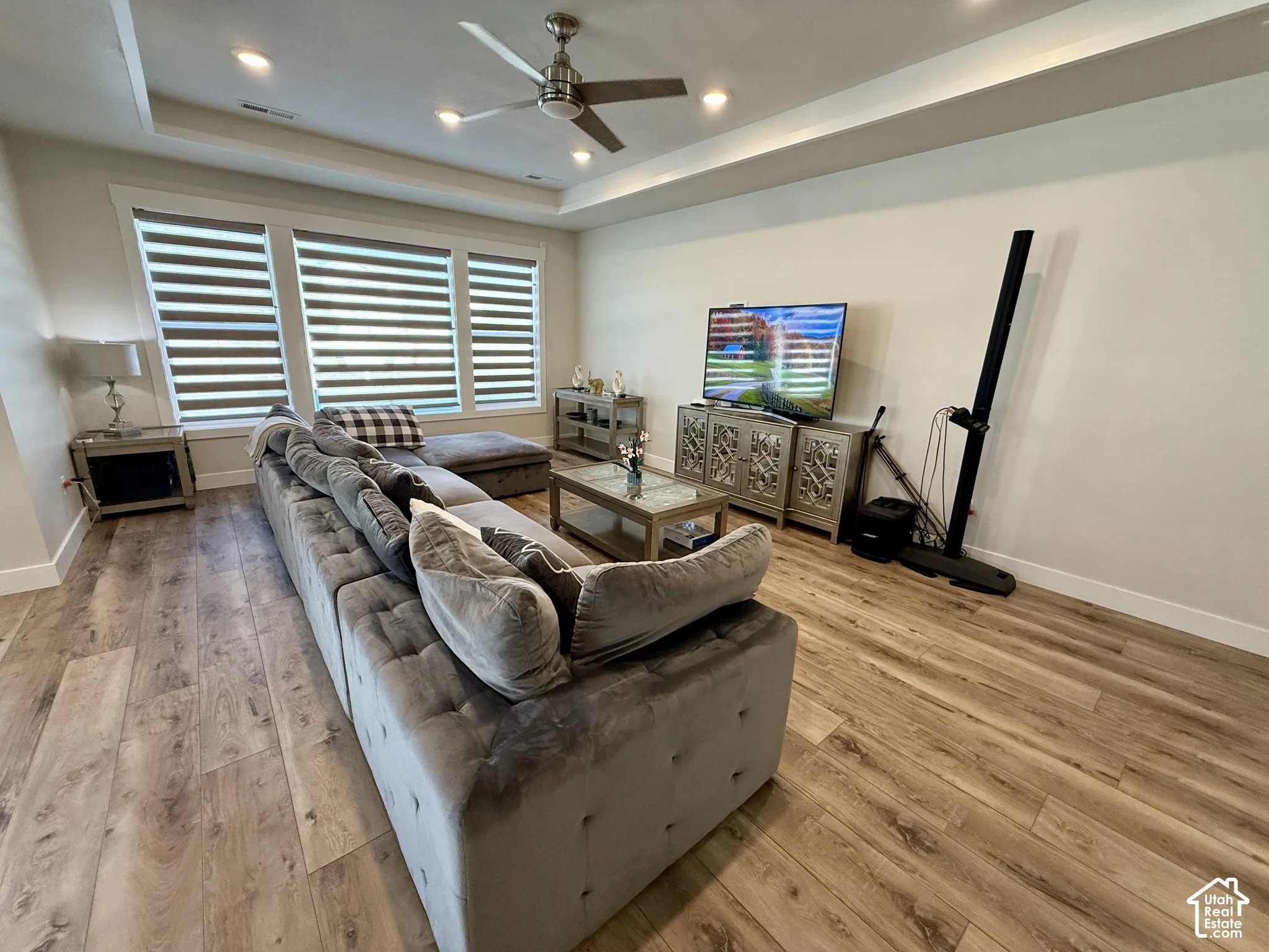 Wood-finish flooring, recessed lighting, ceiling fan, tray ceiling, and white trim