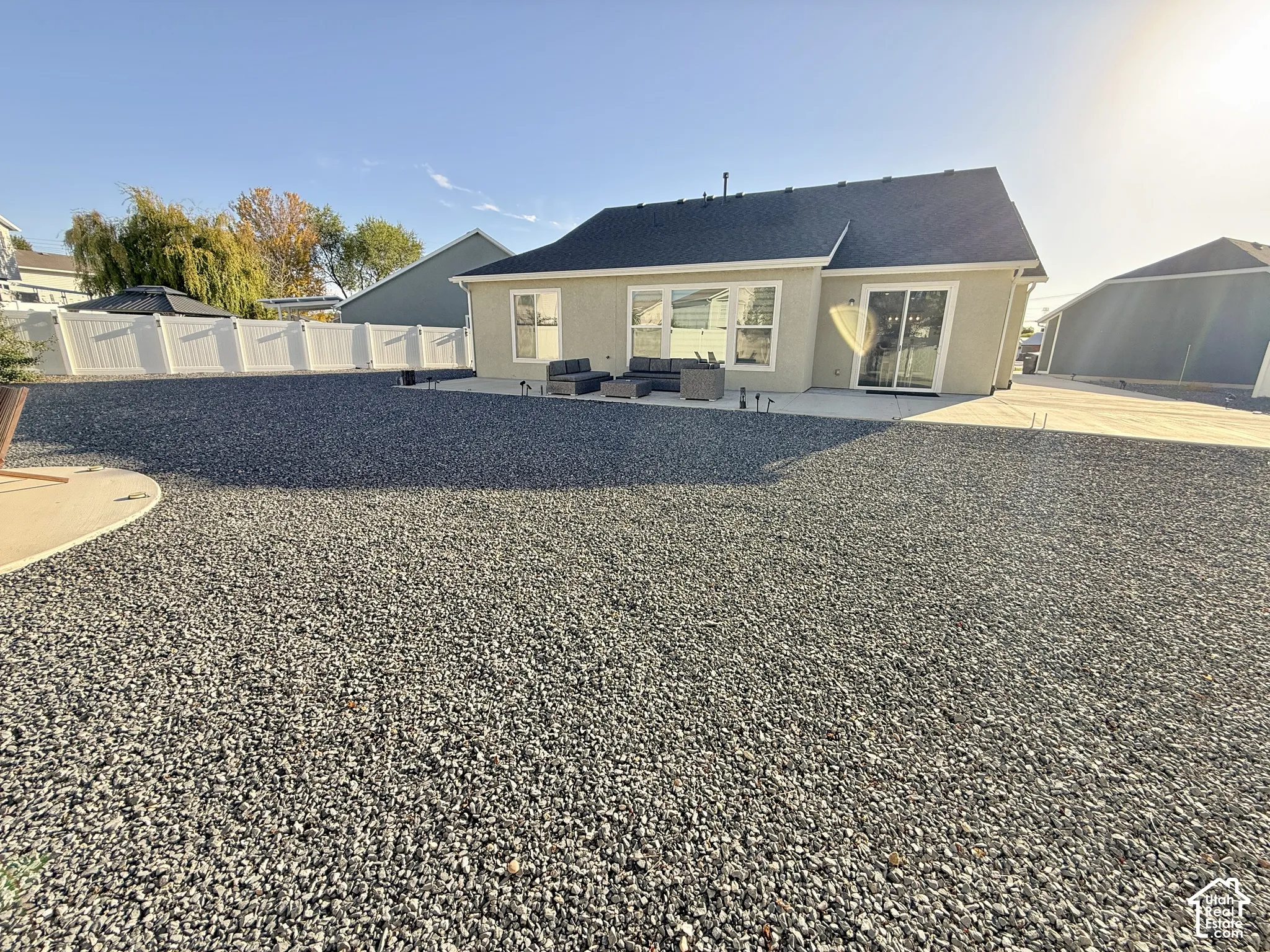 Expansive gravel landscaping with a concrete patio, white vinyl fencing, and a neutral-toned exterior with a dark shingle roof