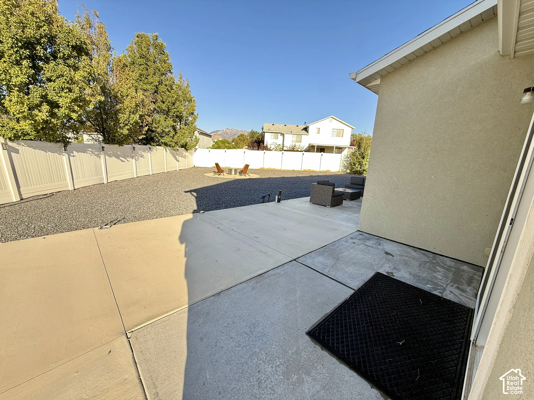Expansive backyard featuring a concrete patio, gravel landscaping, and a white privacy fence