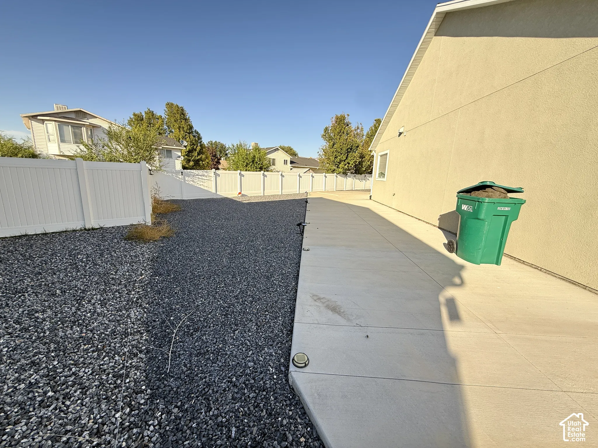 Poured concrete walkway, stucco exterior, white privacy fencing, and a gravel ground cover