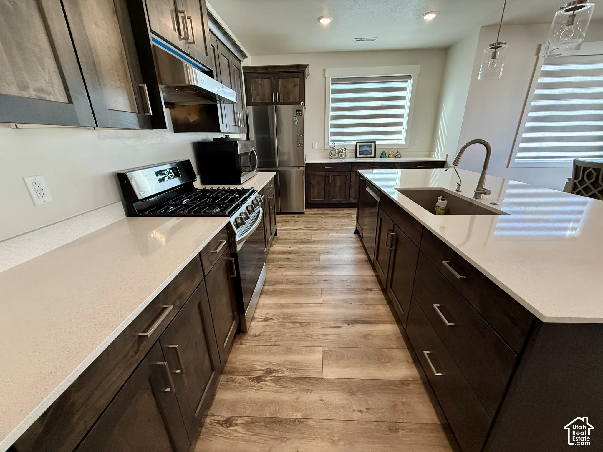 Kitchen with wood-finish flooring, dark wood cabinetry, white countertops, stainless steel appliances, and an island with an undermount sink