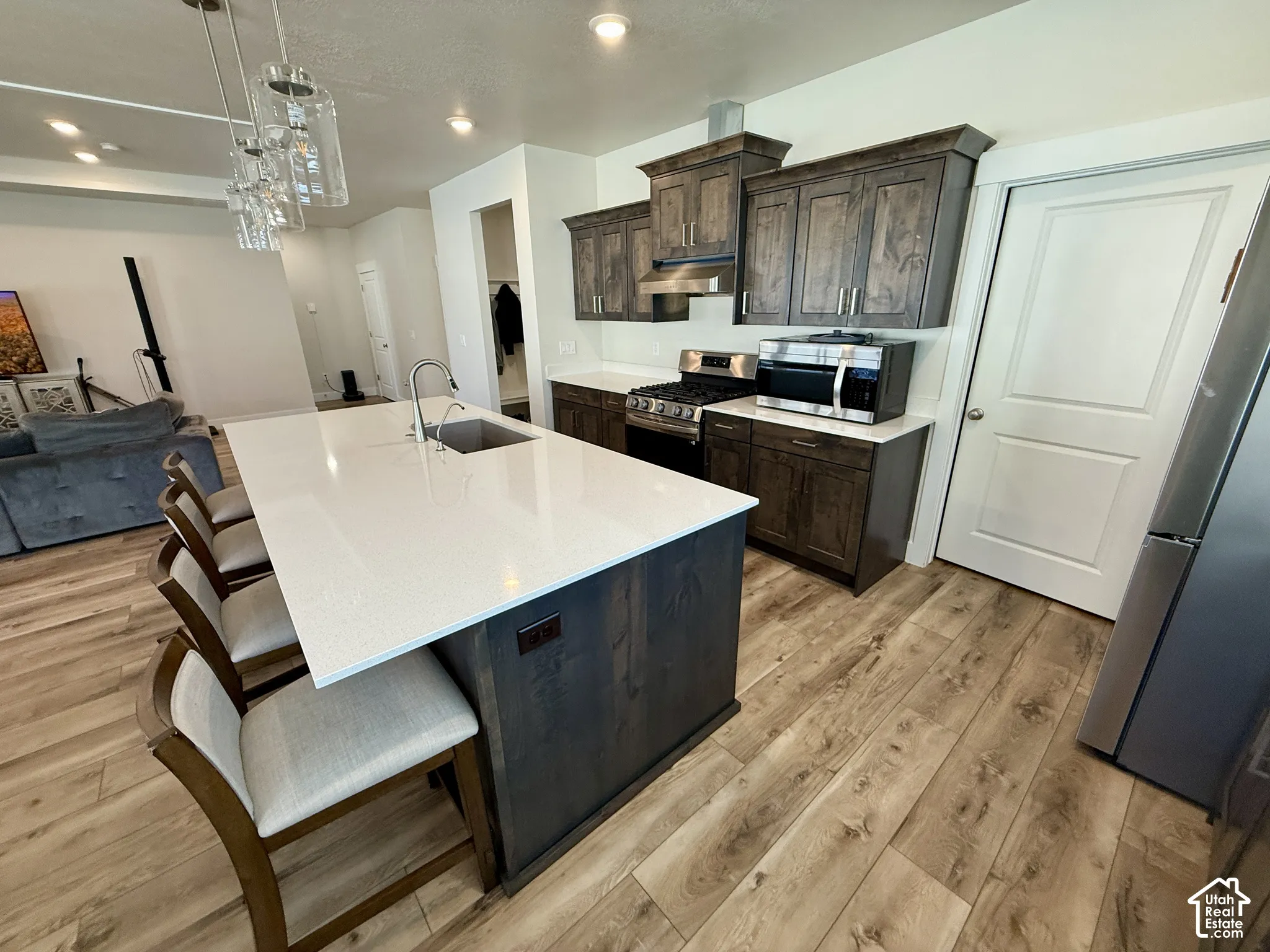 Kitchen featuring an island with a light-toned countertop, wood-finish flooring, dark wood-finish cabinetry, and stainless steel appliances