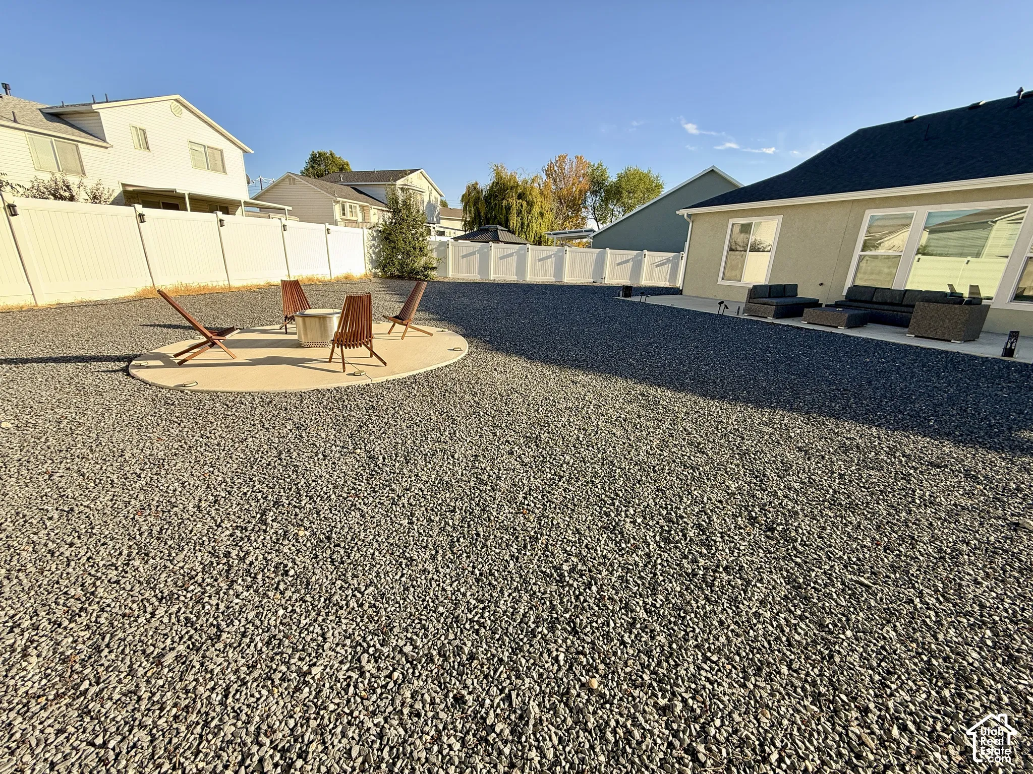 Expansive gravel landscaping featuring a concrete patio, integrated fire pit, and durable vinyl fencing