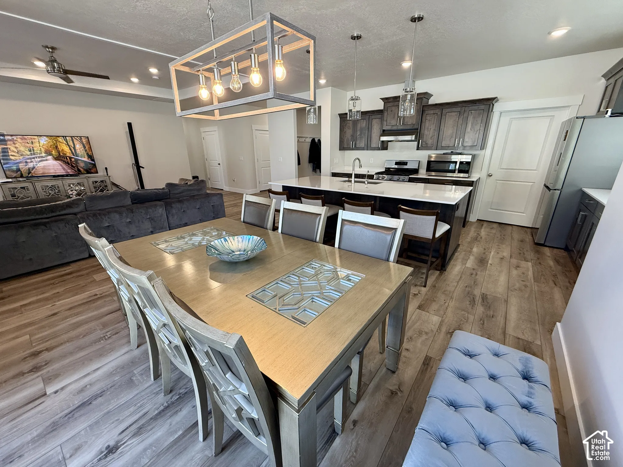 Open-concept living space with wood-finish flooring, a kitchen island with seating, dark wood cabinetry, stainless steel appliances, and recessed lighting