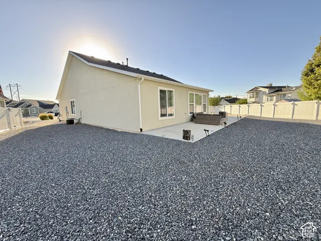 Exterior stucco finish, rear concrete patio, white privacy fencing, and gravel landscaping