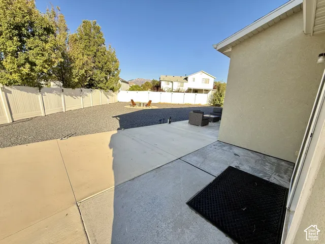Expansive backyard featuring a concrete patio, gravel landscaping, and a white privacy fence