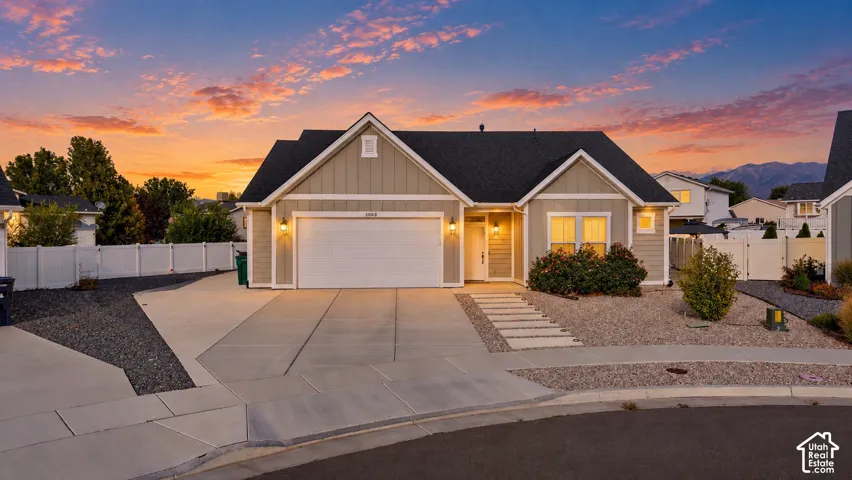Contemporary exterior with light beige siding and dark roof shingles, featuring a concrete driveway, integrated garage, and a landscaped front yard with decorative gravel and mature plantings