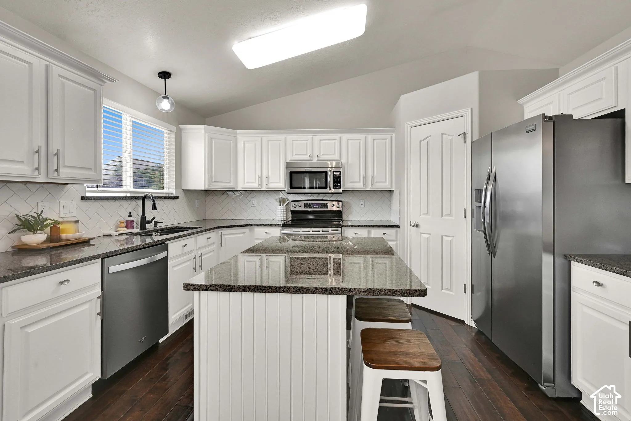 White cabinetry with brushed nickel hardware, dark wood flooring, stainless steel appliances, granite countertops, and white tile backsplash