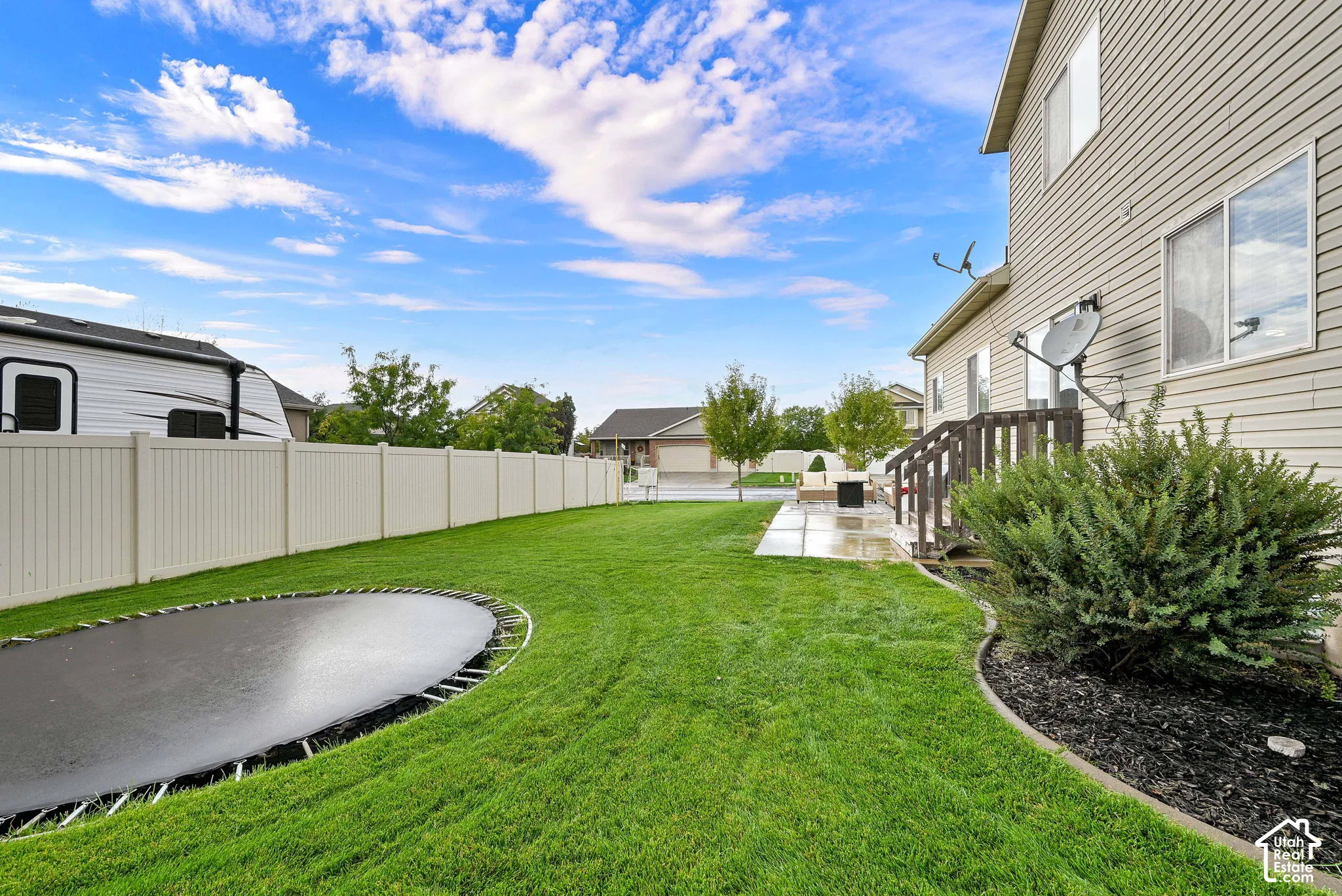 Expansive backyard featuring a manicured lawn, a ground-level patio, and wood stairs to access the residence
