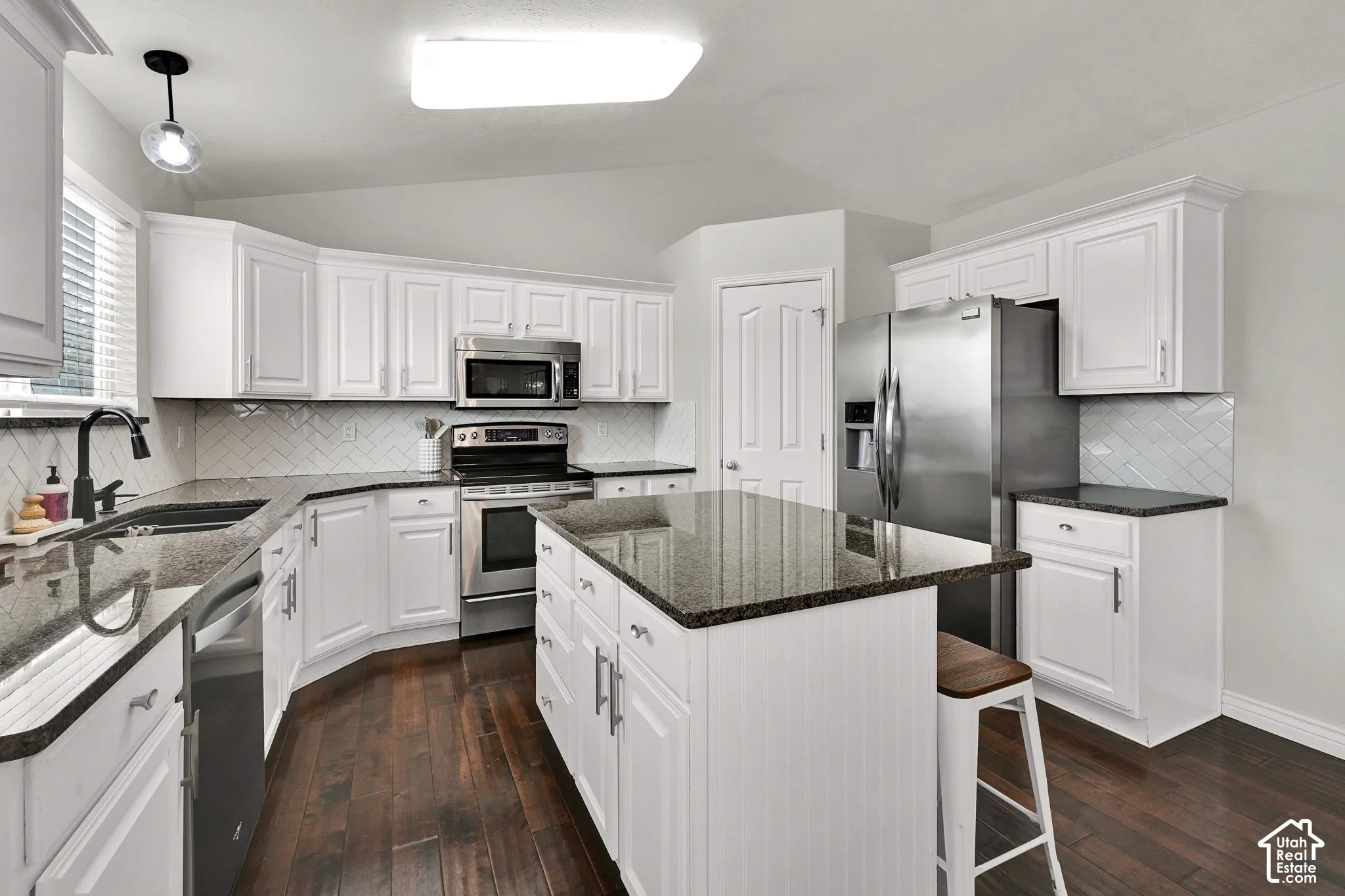 Kitchen featuring white cabinetry, stainless steel appliances, dark stone countertops, wood flooring, and an island with seating