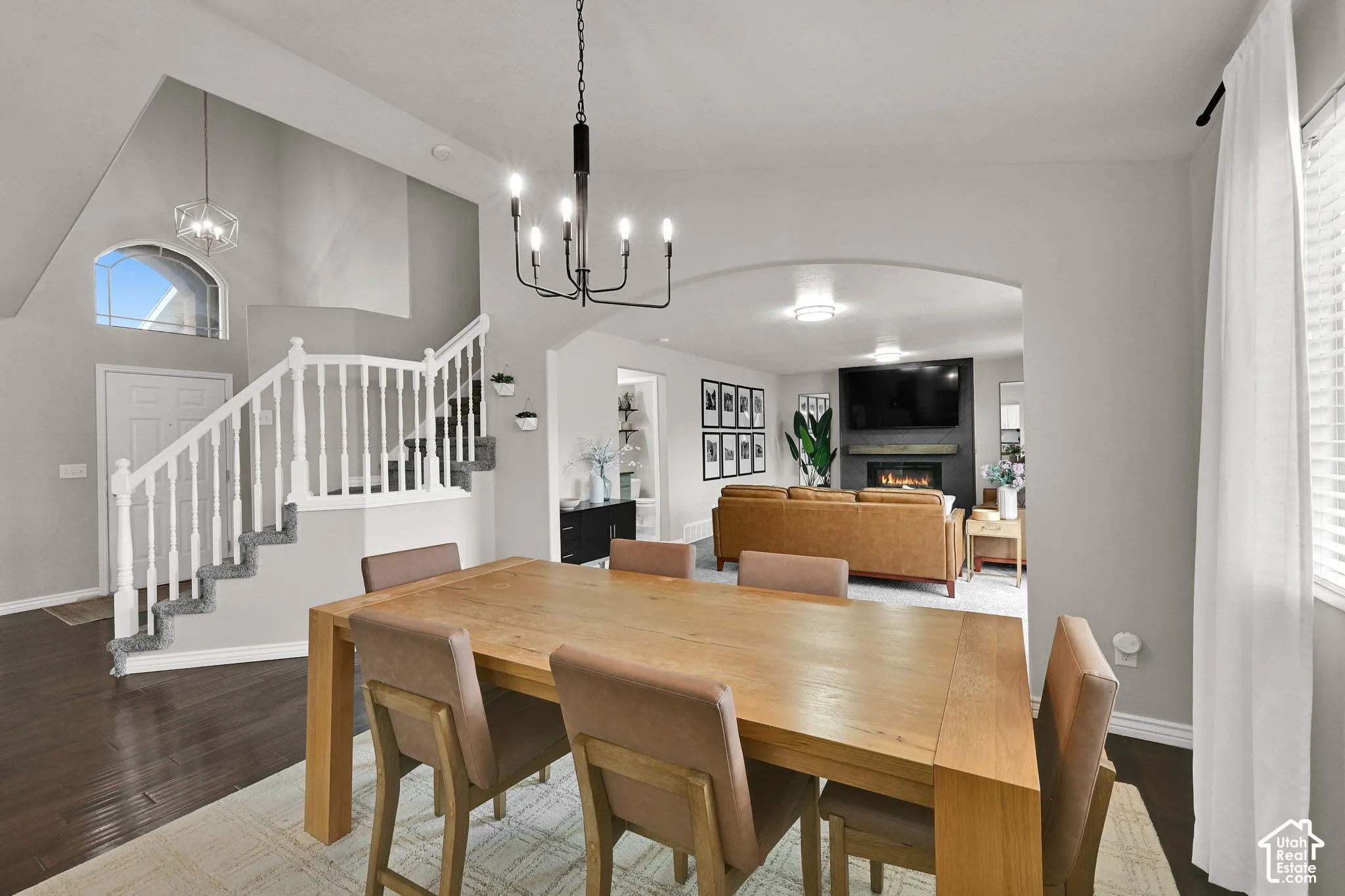 Vaulted ceilings, a prominent staircase with white balusters, wood flooring, beautiful archway, and a modern chandelier
