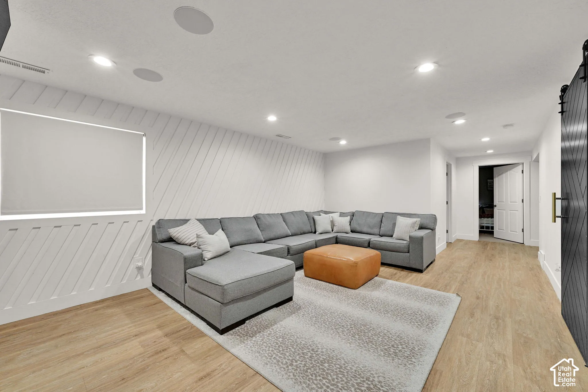 Recessed lighting, wood-finish flooring, accent wall with diagonal paneling, built-in ceiling speakers, and a barn door