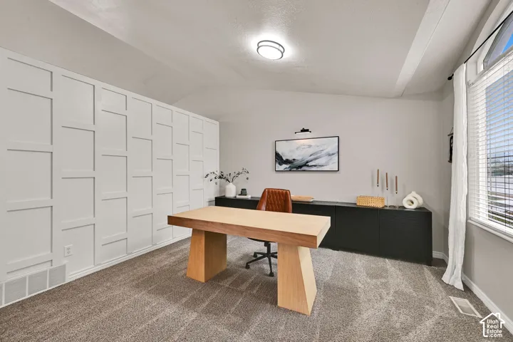 Accent wall with geometric paneling, large window with drapes, vaulted ceiling, and carpeted flooring