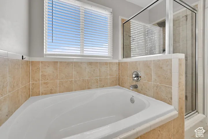 Built-in soaking tub with chrome fixtures, surrounded by light-toned square tile, with a separate glass-enclosed shower