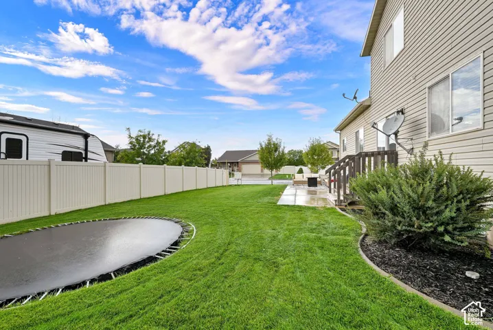 Expansive backyard featuring a manicured lawn, a ground-level patio, and wood stairs to access the residence