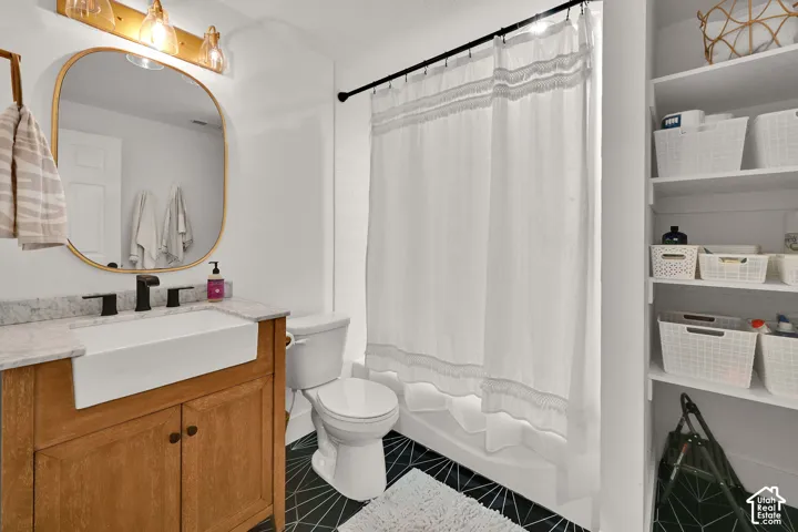 Bathroom featuring a wood-finish vanity with a farmhouse sink, stone countertop, and matte black fixtures