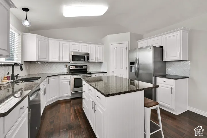 Kitchen featuring white cabinetry, stainless steel appliances, dark stone countertops, wood flooring, and an island with seating
