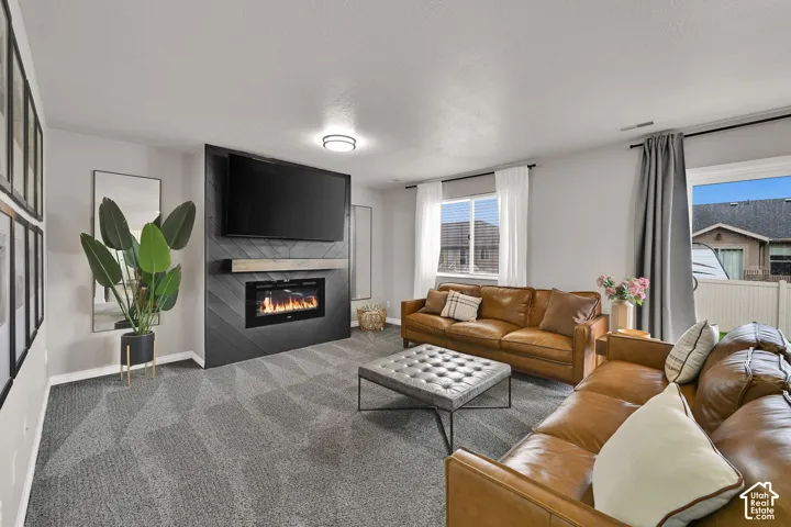 Modern living area featuring a fireplace with a chevron-patterned surround, a natural wood-finish mantel, and carpeting