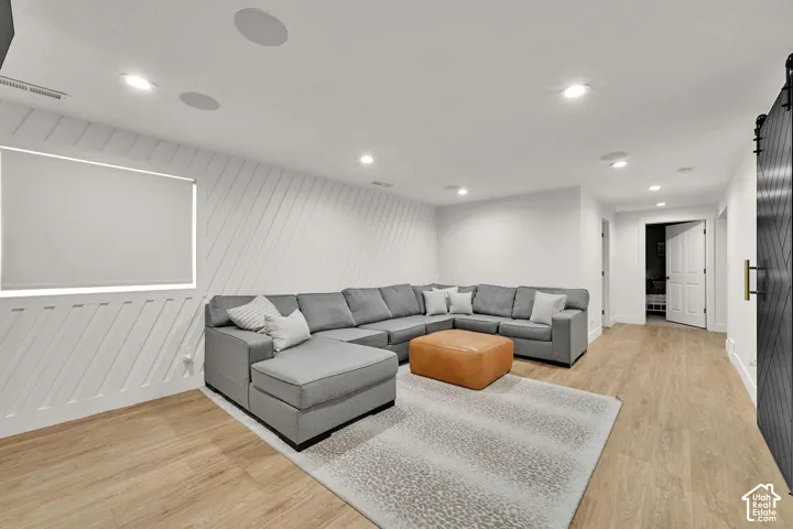 Recessed lighting, wood-finish flooring, accent wall with diagonal paneling, built-in ceiling speakers, and a barn door