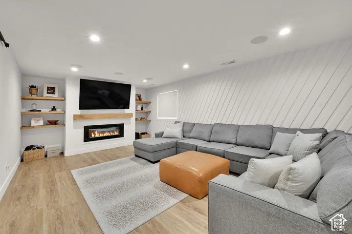 Built-in electric fireplace with a wood mantle, recessed lighting, wood-finish flooring, built-in shelving, and a decorative accent wall