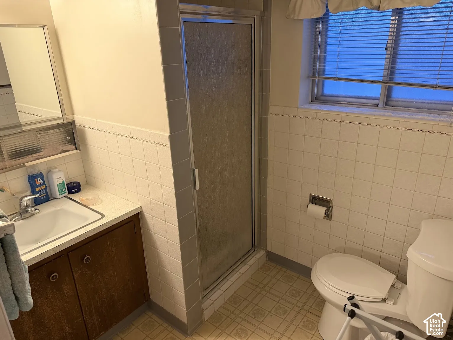 Bathroom featuring a shower enclosure, white square wall tiling, and a window with blinds