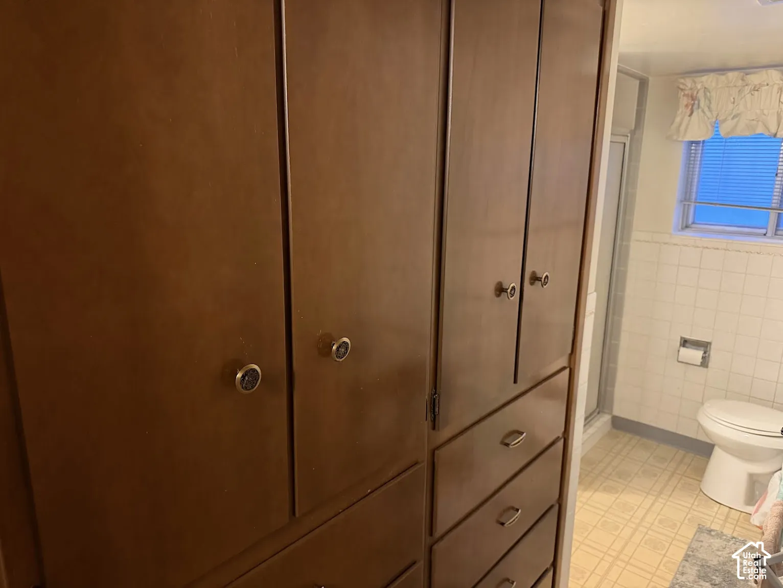 Built-in wood-finish cabinetry with multiple drawers and doors, tile-pattern flooring, and a white toilet