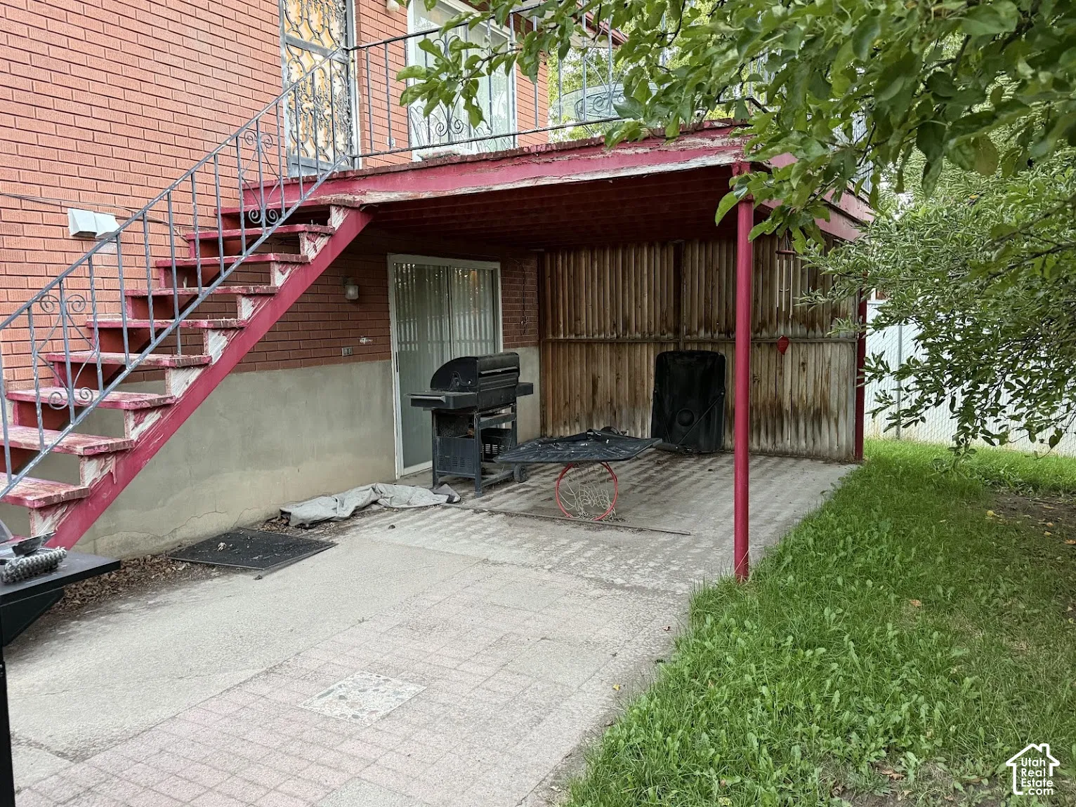 Brick exterior with exterior staircase featuring wrought iron railing, concrete patio, and covered outdoor area